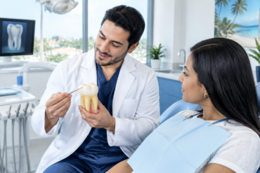 Odontólogo explica a una paciente cómo comienza la caries usando un modelo dental.
